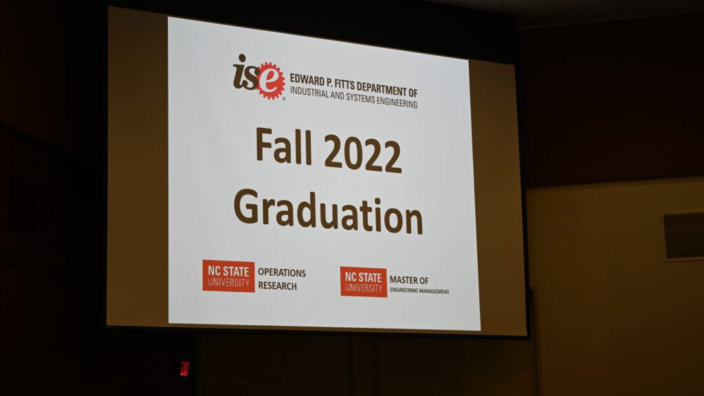 A large projection screen with the word Fall 2022 Graduation with the logos from the ISE, OR and MEM programs
