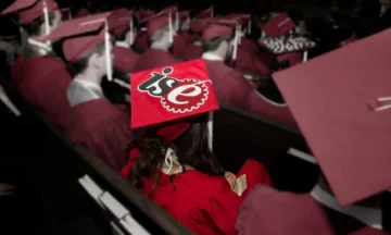 Rows of students at graduation with one student being highlighted as she wears the ISE logo on her cap.