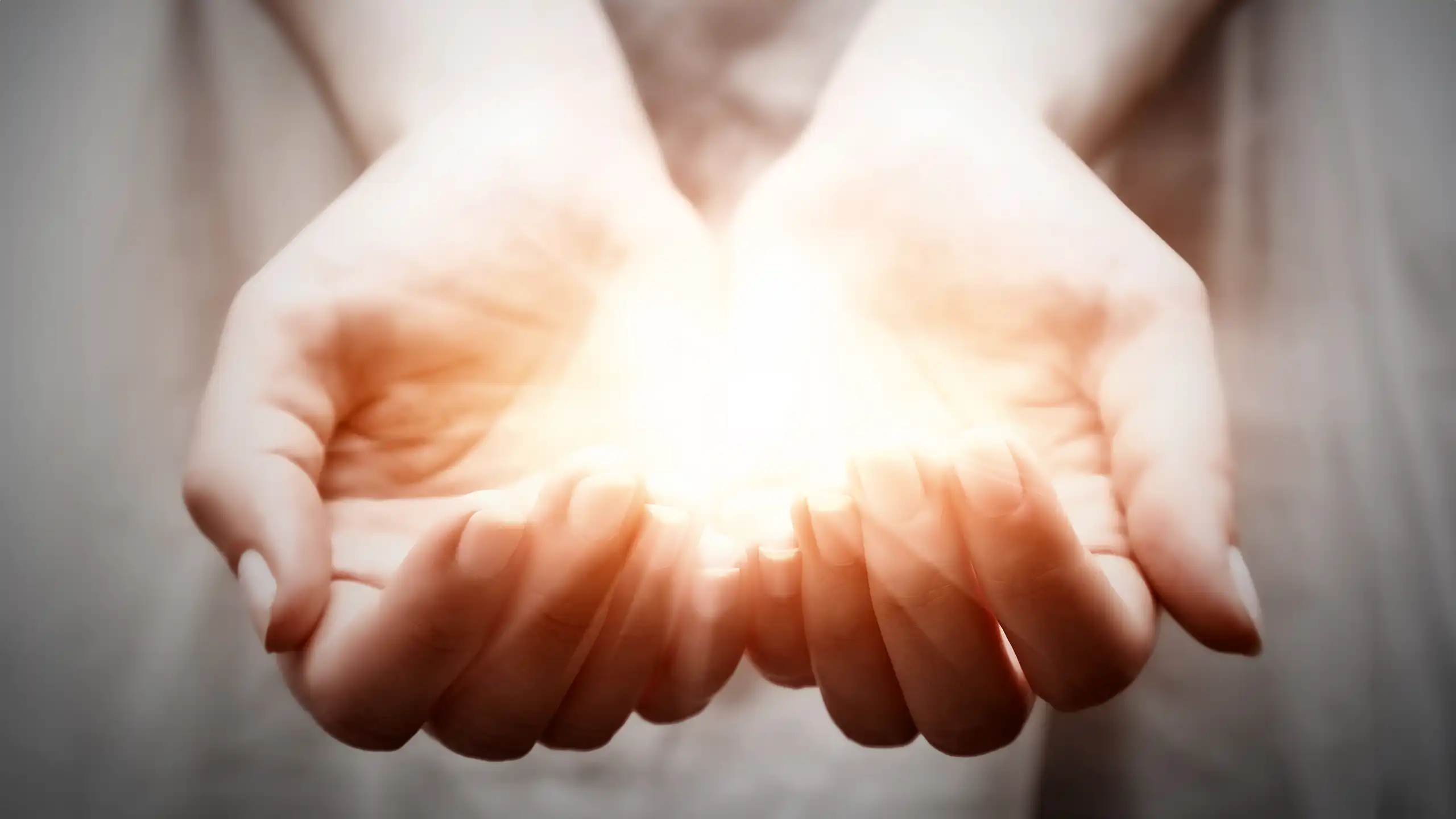 Two cupped hands holding a glowing object.