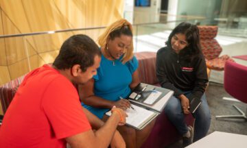 Latha Dombro, student services coordinator, sitting on a couch with two MEM Students discussing their schedules