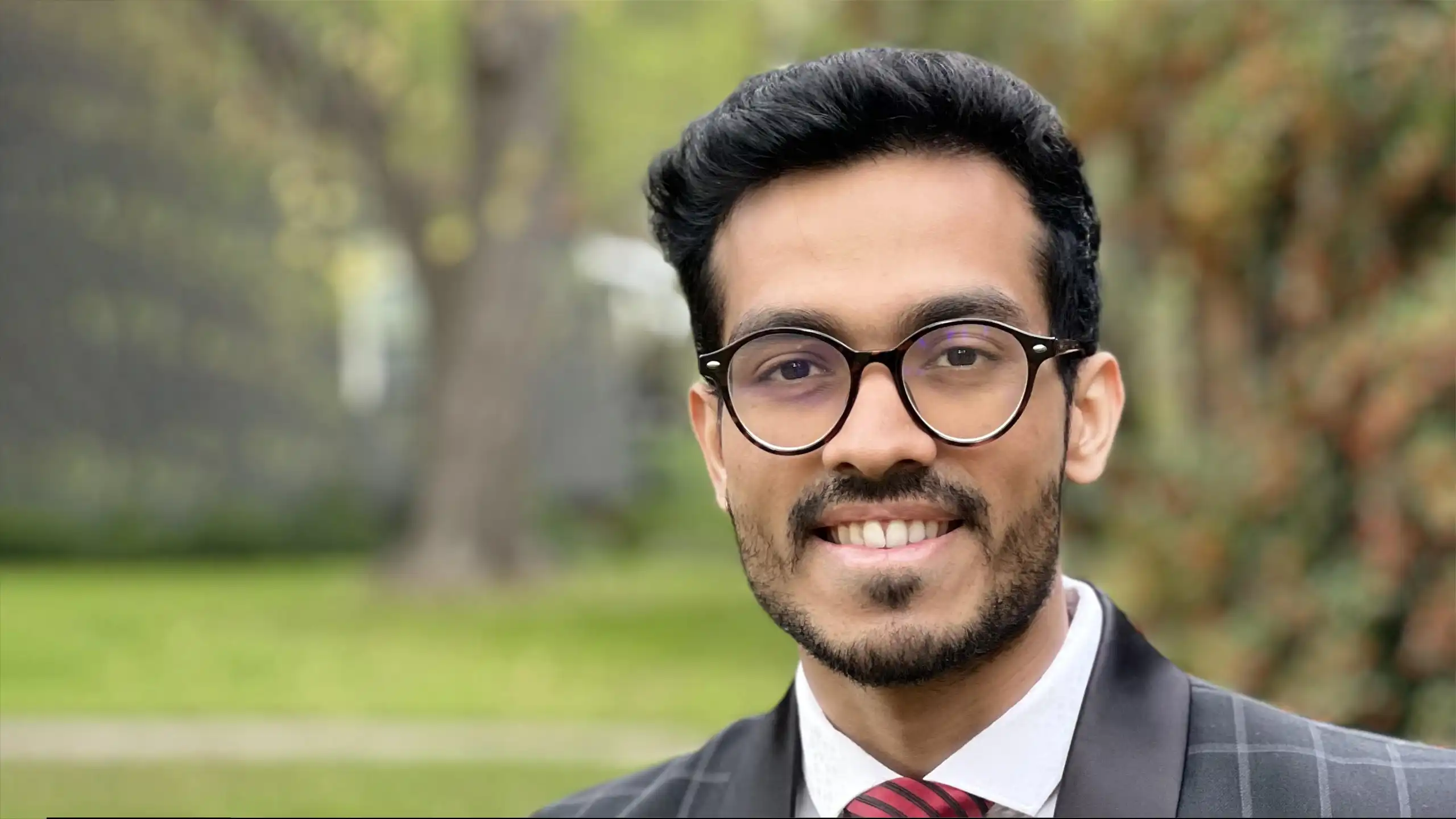 A headshot of Abhijay Shukla standing outside in front of some trees.