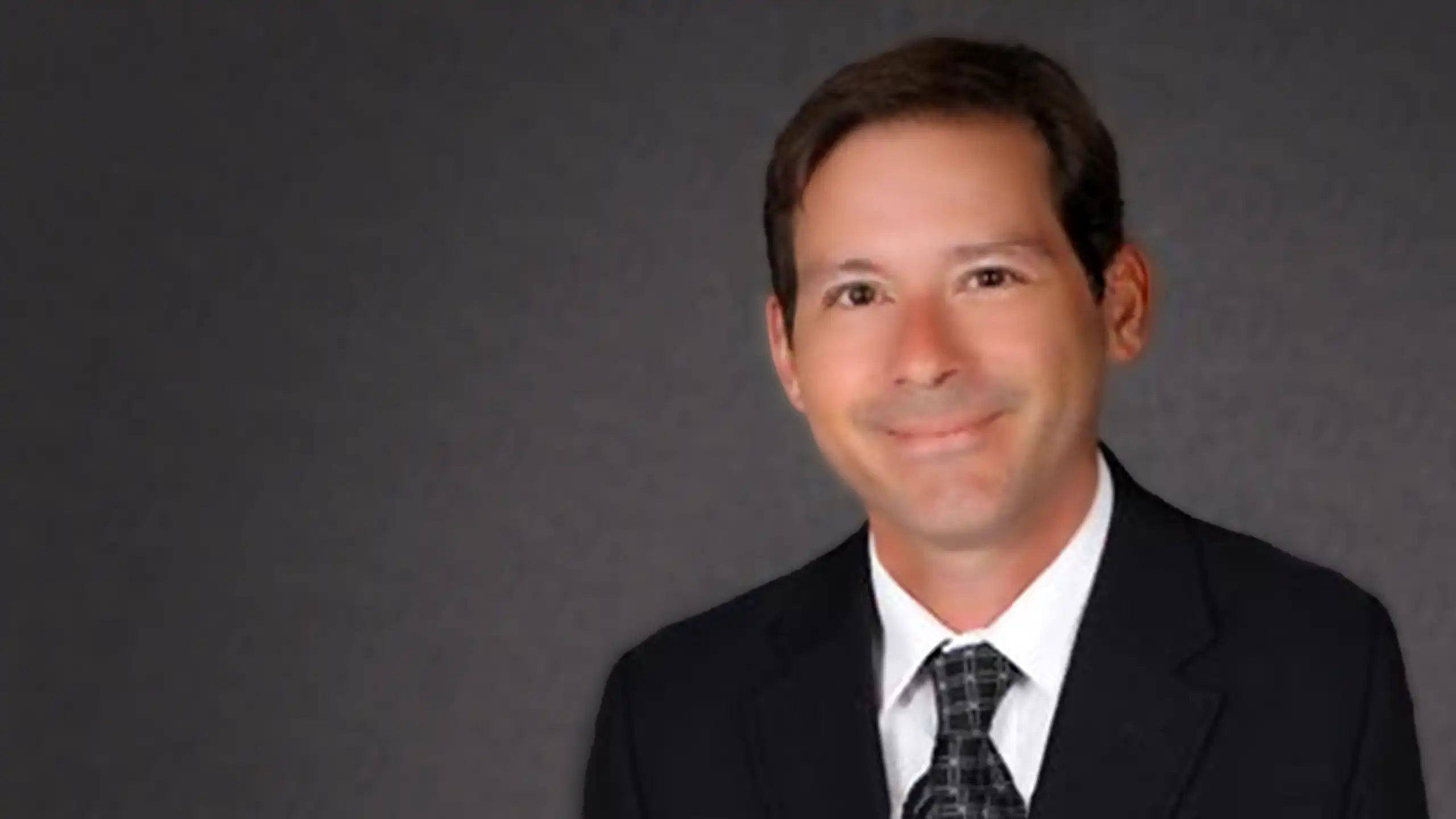 A headshot of Christopher Rock standing in front of a dark gray background.