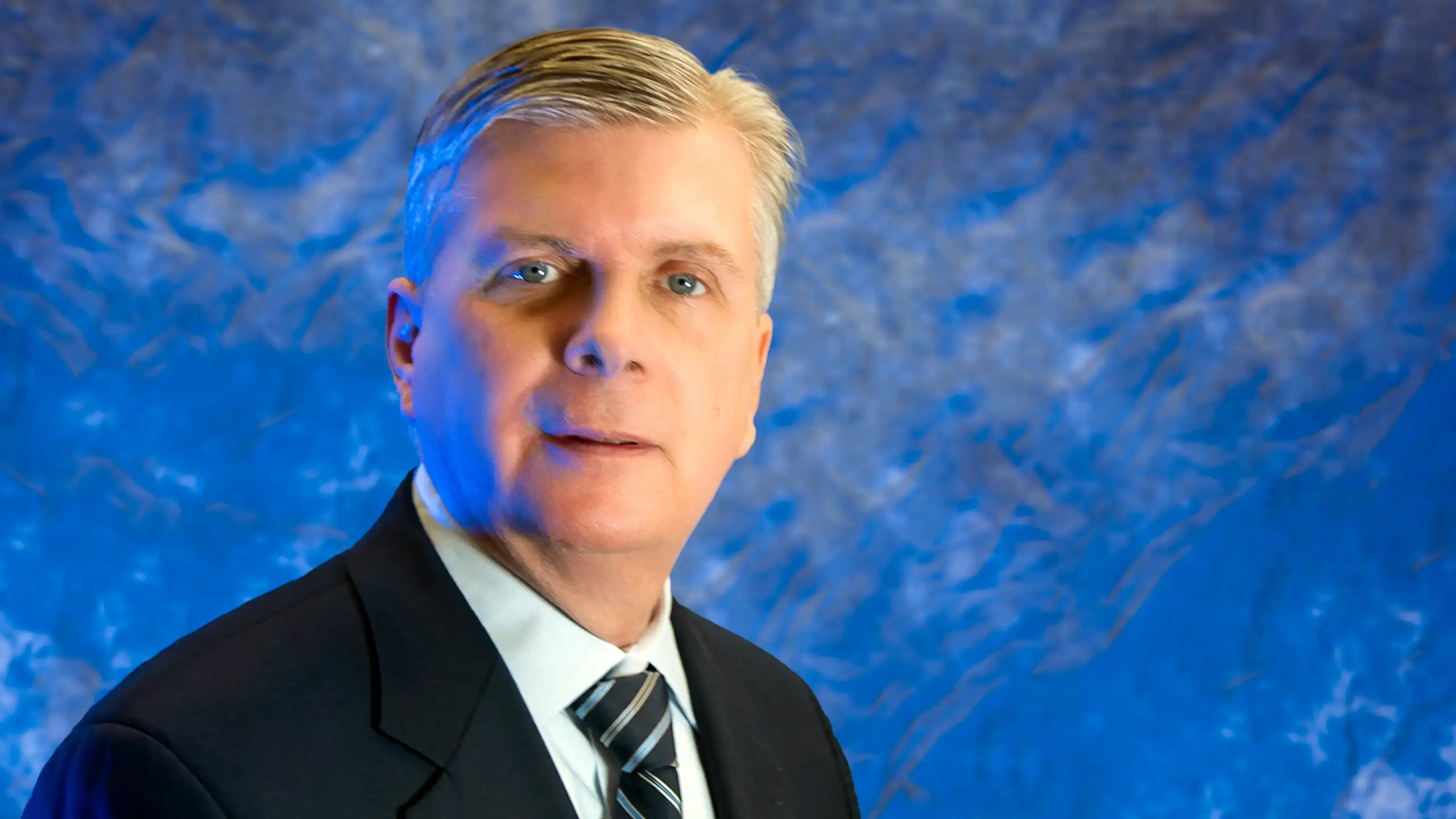 A headshot of Patrick Murray standing in front of a blue background.