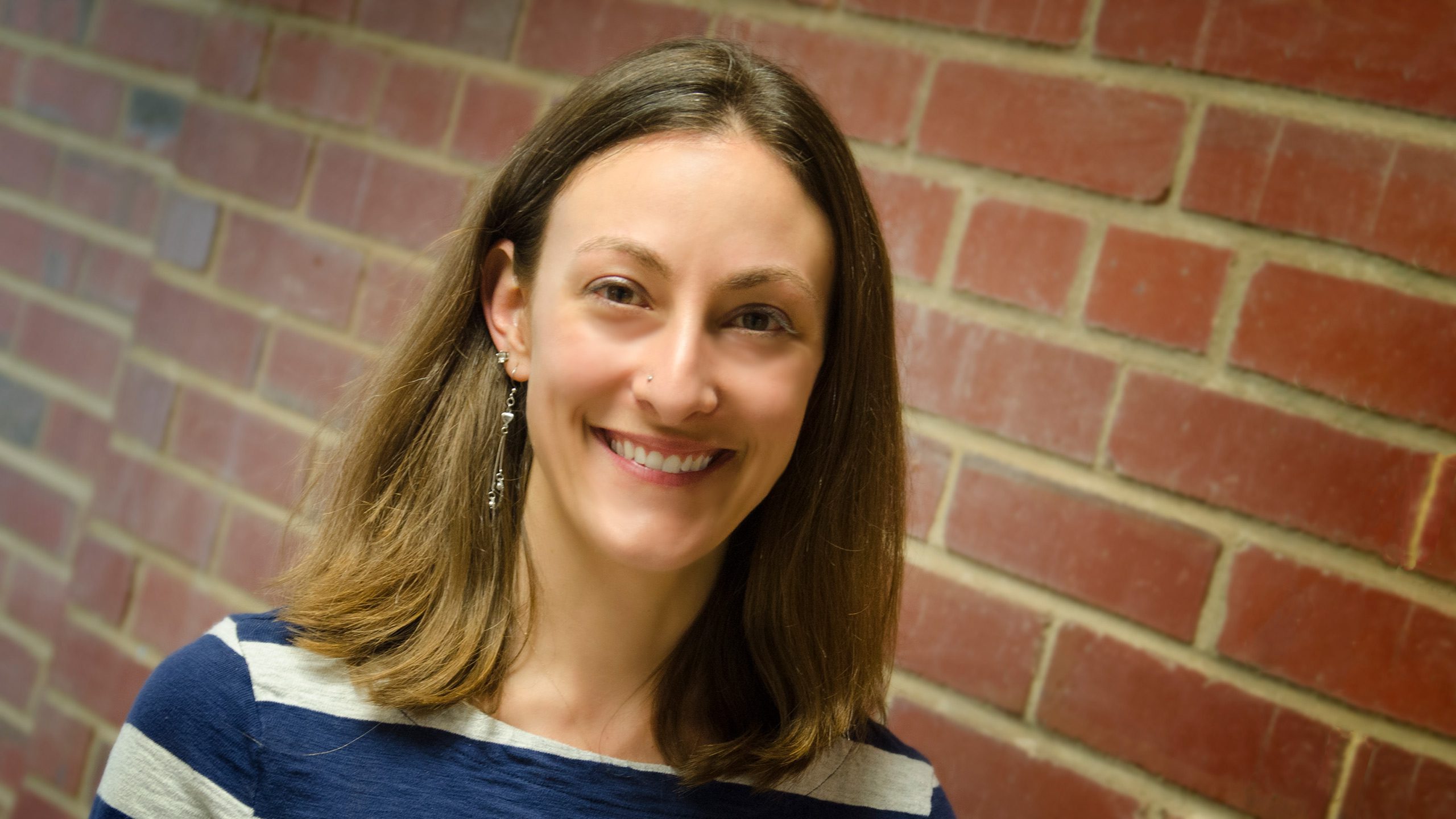 A headshot of Anita Vila-Parrish standing in front of a brick wall.