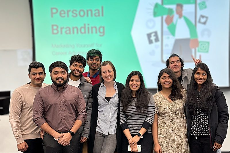 Guest speaker Sarah Glova standing with a group of students in front of her presentation