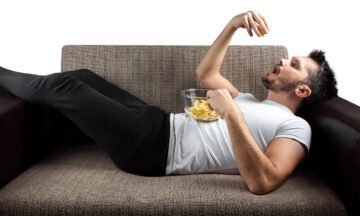 A man laying on a couch eating chips