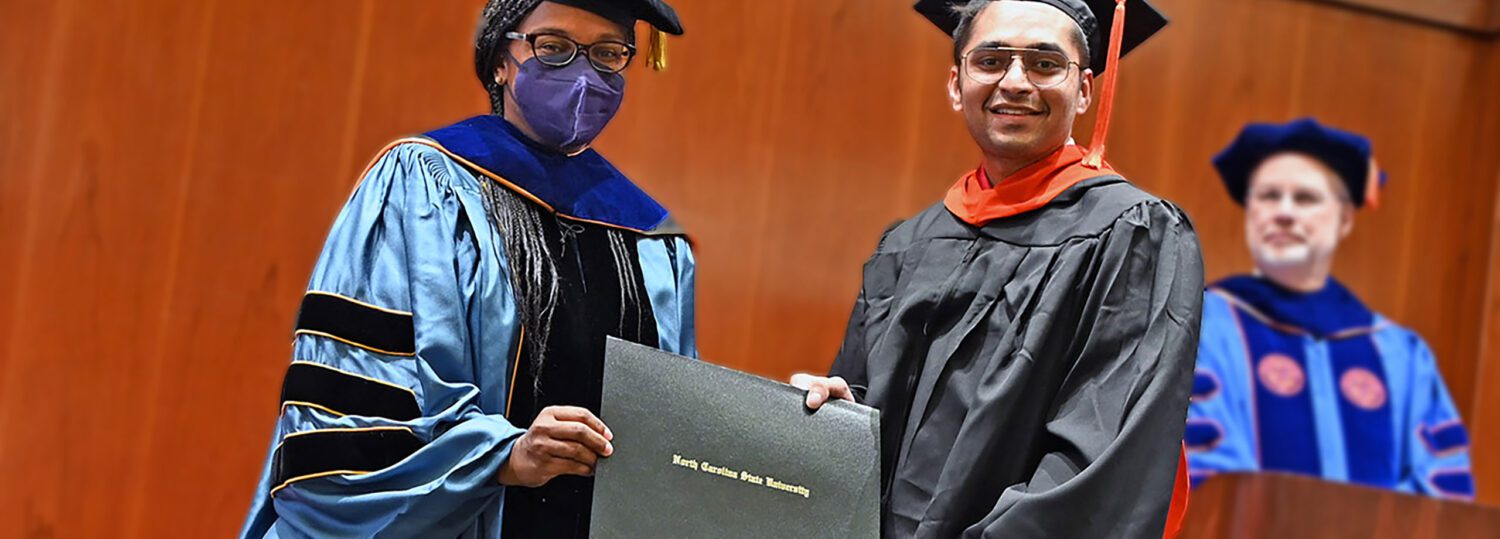 Two people in graduation regalia holding up a diploma