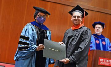 Two people in graduation regalia holding up a diploma