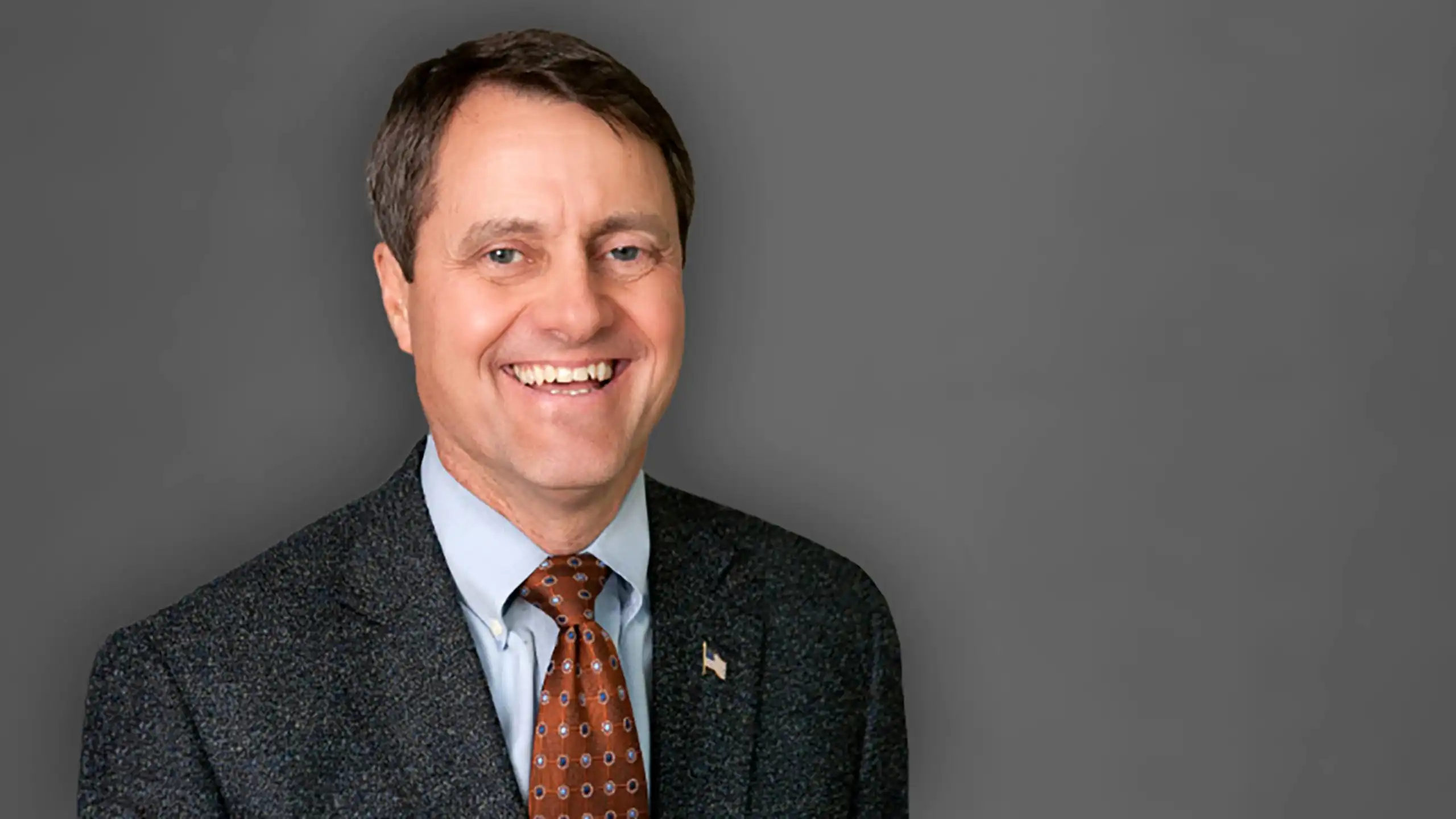 A headshot of George Auten standing in front of a gray background.