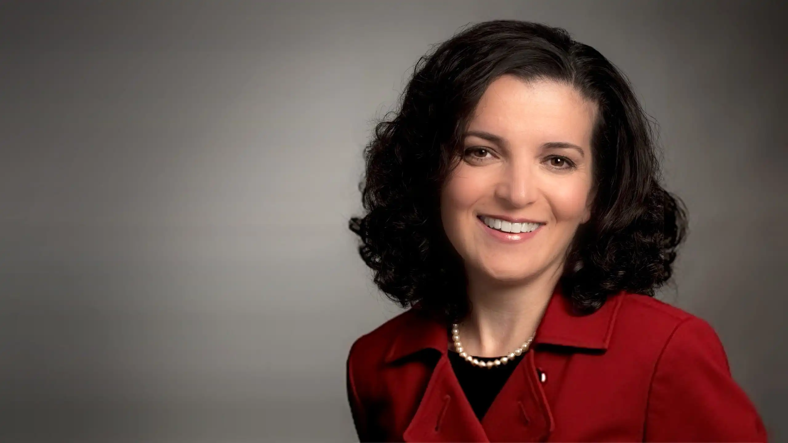 A headshot of Elif Oker standing in front of a medium gray background.