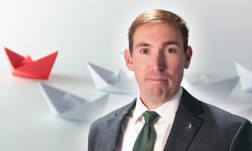 Brandon McConnell, the new MEM Director, standing in front of many paper boats that are being led by one red boat.