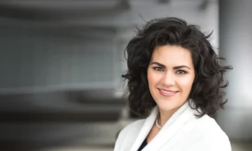 A headshot of Anne Moorer standing in front of a glass wall.