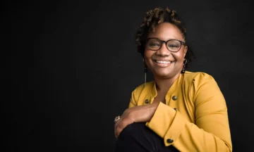 A headshot of Rashida Hodge in front of a black background.