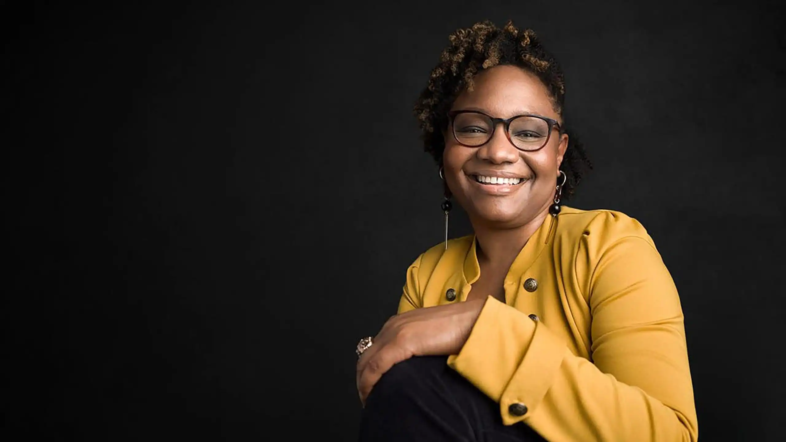 A headshot of Rashida Hodge in front of a black background.