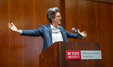 Link Neal standing behind the podium with his arms spread out wide.