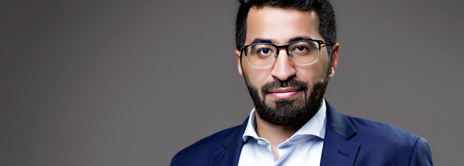 A headshot of Hassan Almuzel in front of a gray background