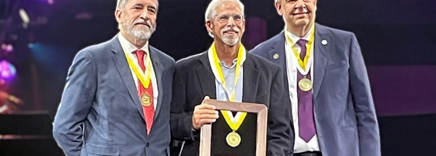 Steve DelGrosso on stage holding his Fellow Award with a PMI officer on each side of him.