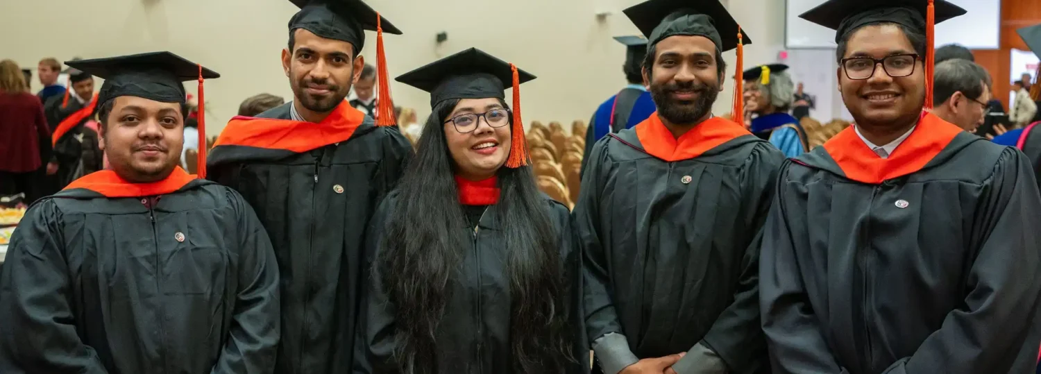 Five graduate students stand together in their graduation caps and gowns.