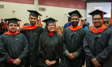 Five graduate students stand together in their graduation caps and gowns.