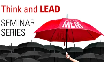 A large red umbrella with the words "NC State MEM" printed on it heard above a sea of smaller black umbrellas. In the background are the words Think and Lead Seminar Series.