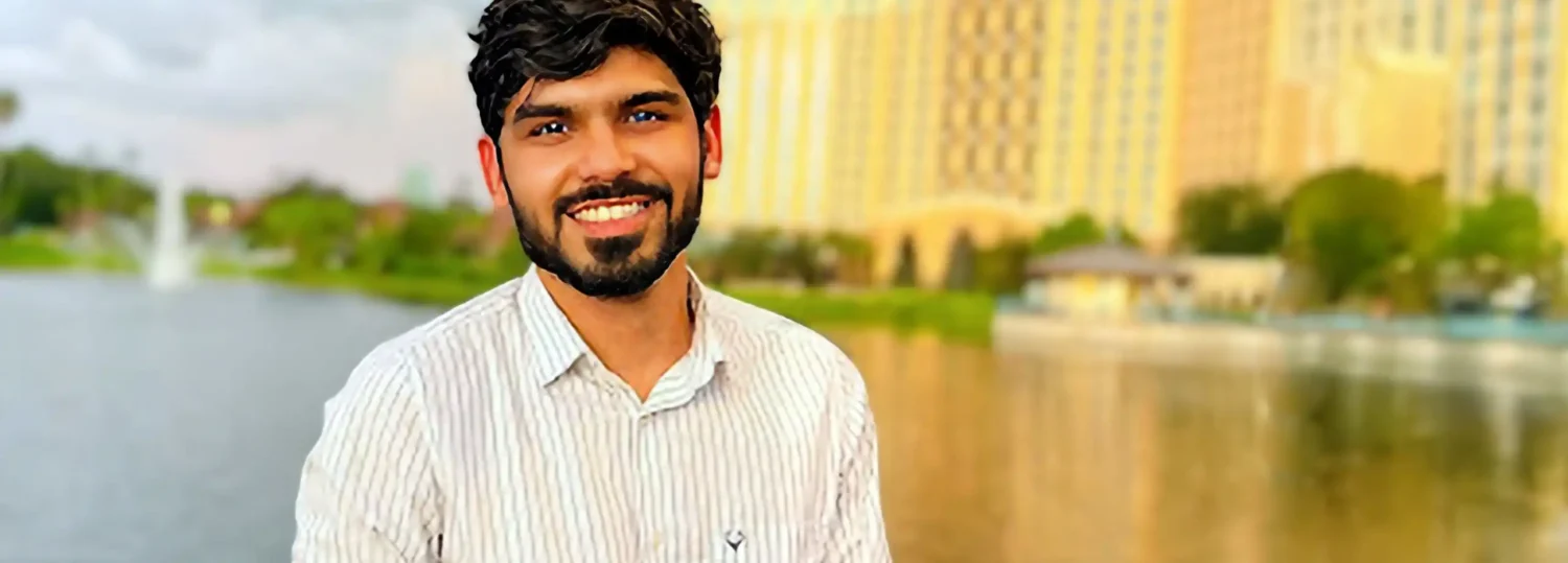 Dwij Bharadwaj stands on a bridge in front of a lake and a hotel