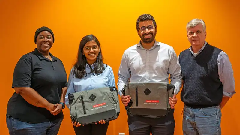 Hassan Almuzel and Goldan Azhagappaselvan hold their first place prize, a dufflebag, while standing between Alum Tammy Montgomery and ISE's Patrick Murray.