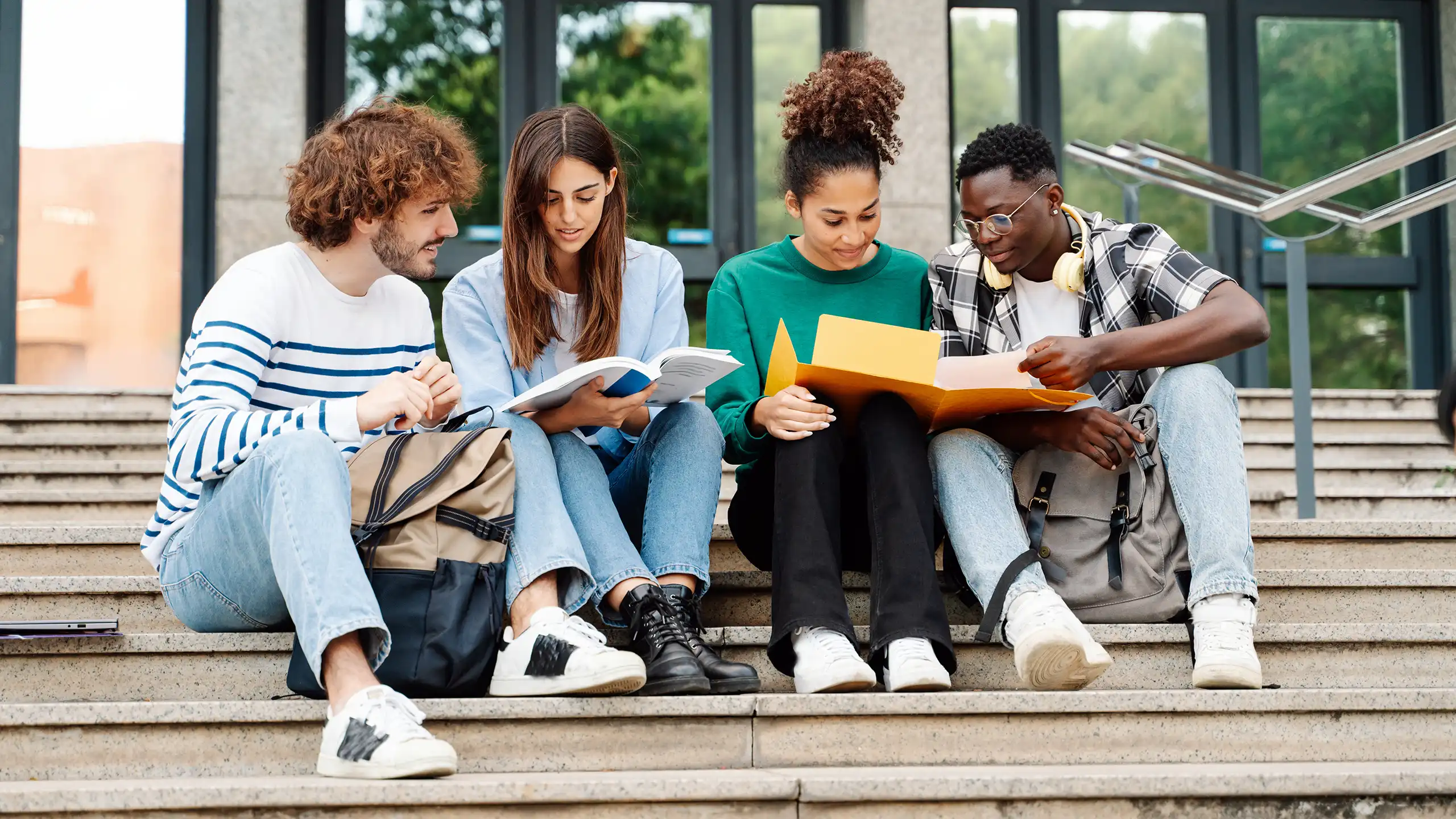 Four on-campus students sitting on the steps outside of a large building after their on-campus engineering classes.