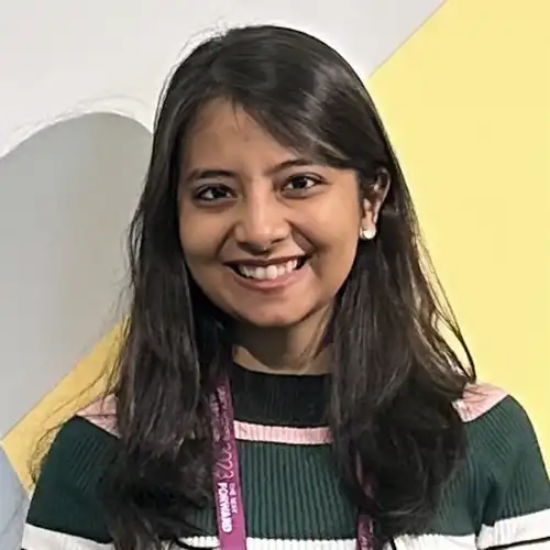 A headshot of Maitreyi Patil standing in front of a gray and yellow wall.