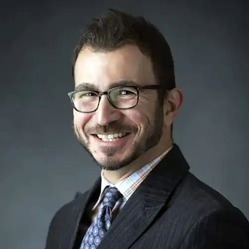 A headshot of Corey Kiassat standing in front of a dark gray background.