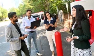 Leila Hajibabai talking with three students while standing in front of an electric car charging station.