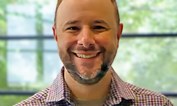 A headshot of Chris Beal standing in front of a large window