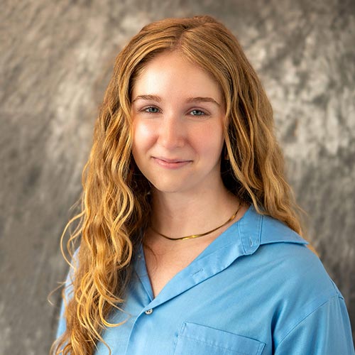 A headshot of MEMbassador Annabel Grocott standing in front of a gray, marbled background.