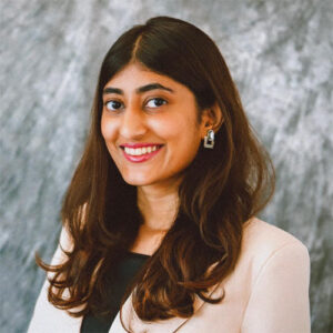 A headshot of Chaitali Shekar standing in front of a gray, marbled background