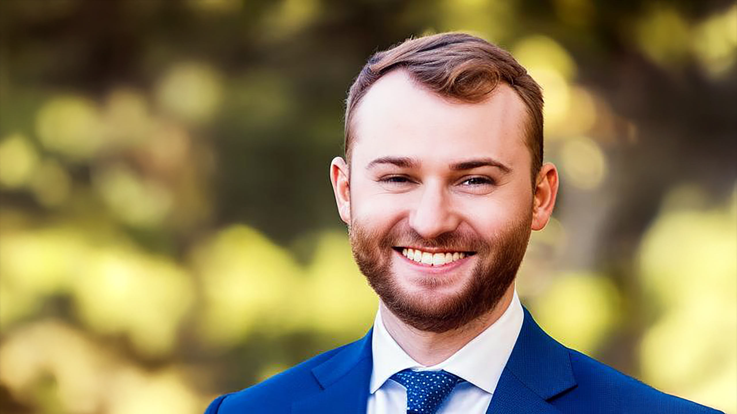 A headshot of Evan Smith standing outside in front of several trees.