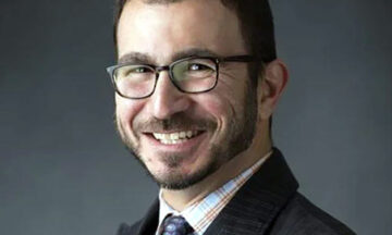A headdshot of Corey Kiassat standing in front of a gray background