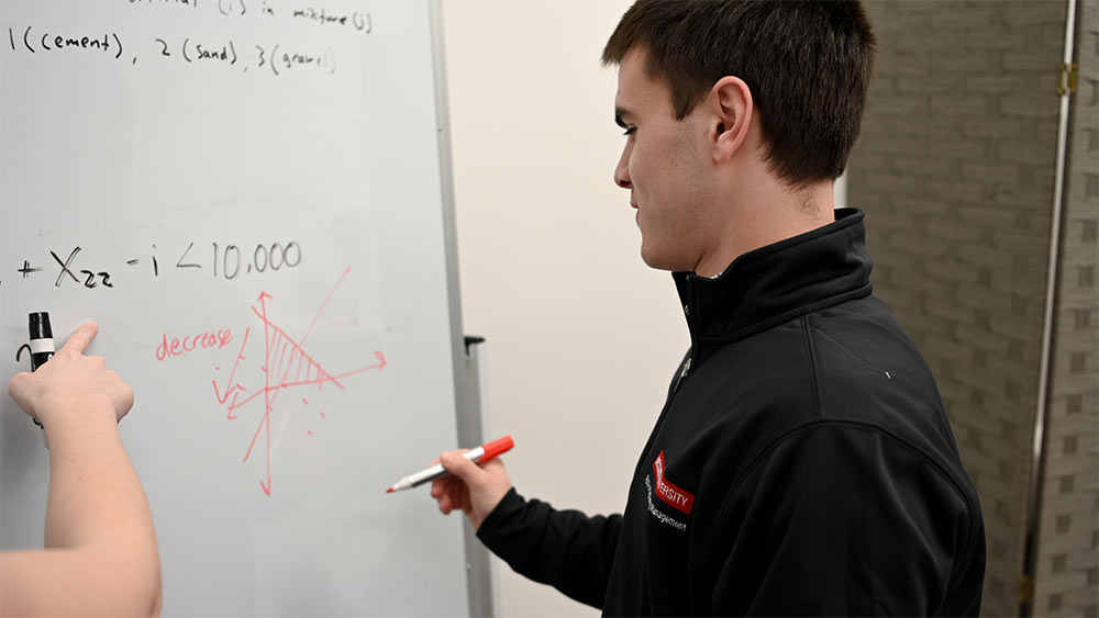 Paul Witmer explains a stats problem on a white board to his study group.
