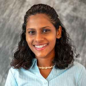 A headshot of Nirmitee Giridhar Keluskar standing in front of a gray, marbled background.